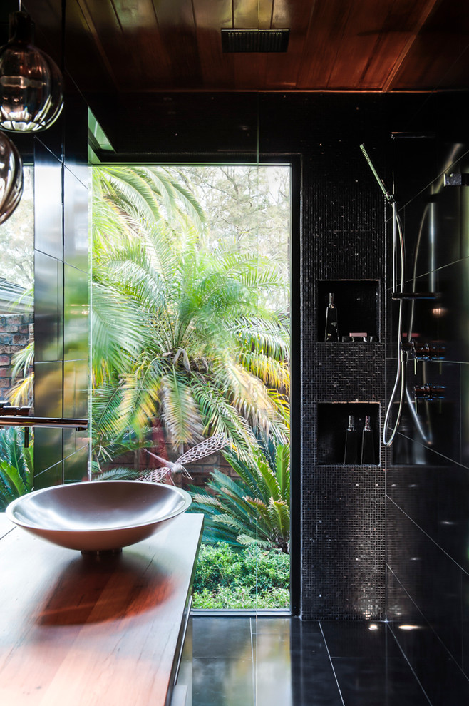 Small modern master bathroom in Sydney with a vessel sink, flat-panel cabinets, white cabinets, wood benchtops, a corner shower, a wall-mount toilet, black tile, mosaic tile, black walls and ceramic floors.