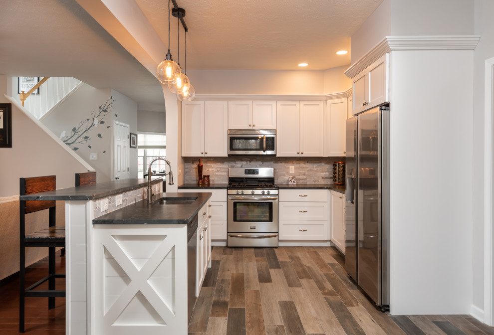 Open concept kitchen - mid-sized rustic l-shaped porcelain tile and gray floor open concept kitchen idea with an undermount sink, shaker cabinets, white cabinets, granite countertops, gray backsplash, brick backsplash, stainless steel appliances, an island and black countertops