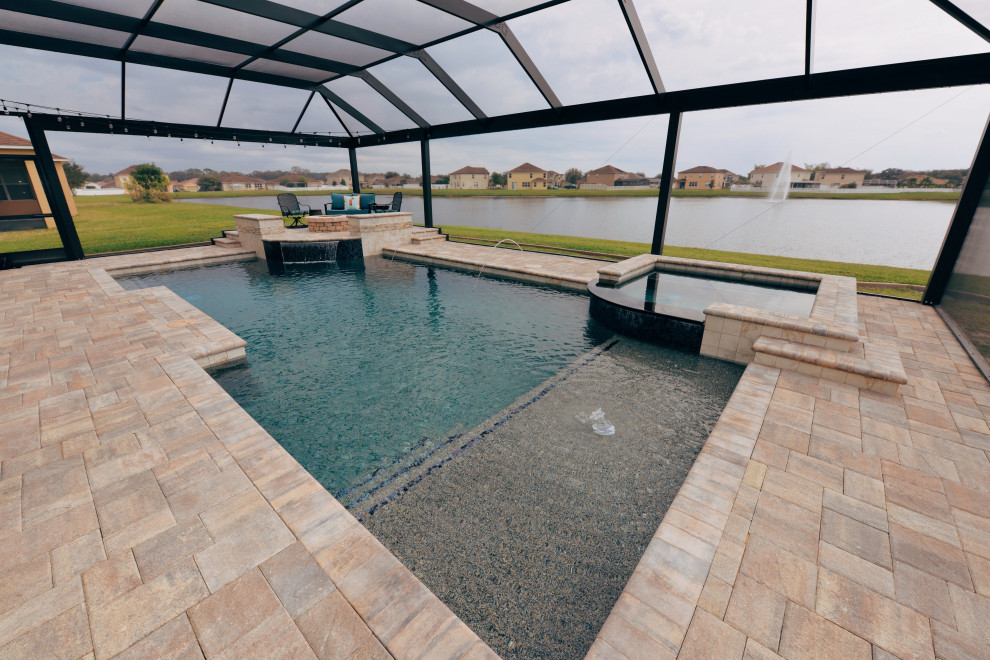This is an example of a large contemporary backyard custom-shaped pool in Orlando with a hot tub and brick pavers.