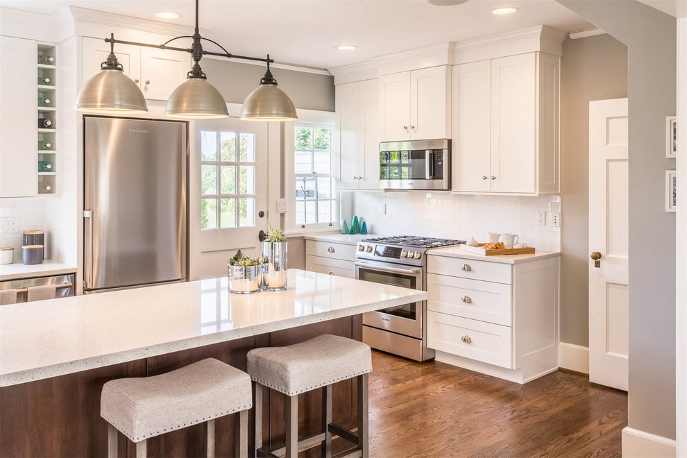 Inspiration for a mid-sized transitional l-shaped open plan kitchen in Seattle with an undermount sink, shaker cabinets, white cabinets, quartz benchtops, white splashback, subway tile splashback, stainless steel appliances, medium hardwood floors and with island.