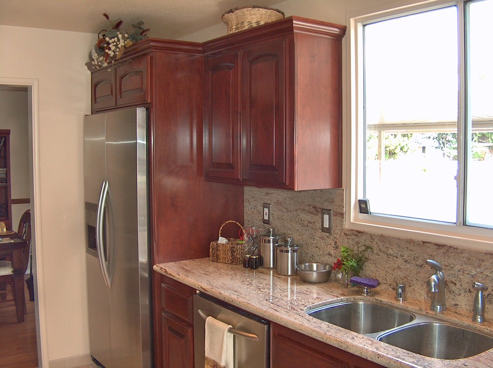 This is an example of a small traditional galley kitchen pantry in Orange County with a double-bowl sink, raised-panel cabinets, dark wood cabinets, granite benchtops, beige splashback, stone slab splashback, stainless steel appliances, ceramic floors and no island.