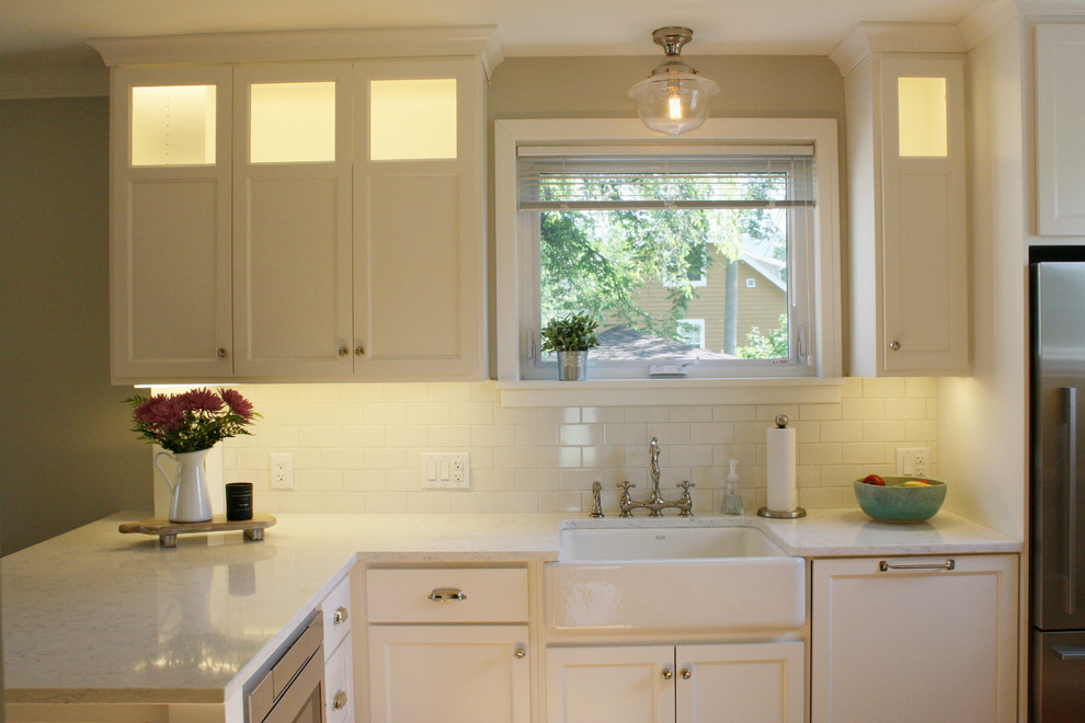 Mid-sized transitional l-shaped kitchen photo with a farmhouse sink, shaker cabinets, white cabinets, quartz countertops, white backsplash, subway tile backsplash, stainless steel appliances and white countertops