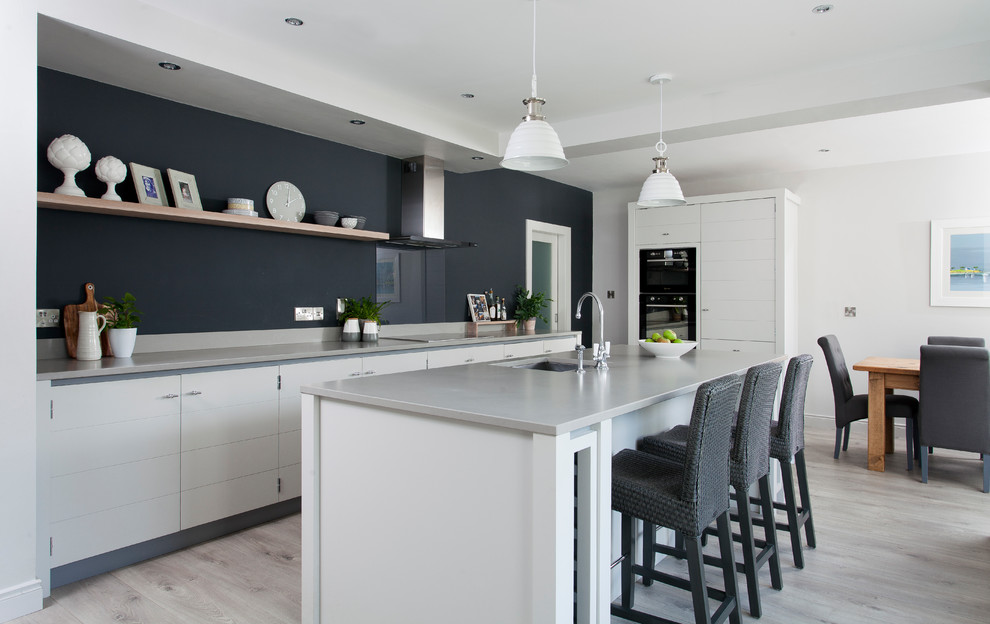 Design ideas for a large transitional single-wall open plan kitchen in Dublin with flat-panel cabinets, white cabinets, light hardwood floors, with island, grey floor, an undermount sink and black appliances.