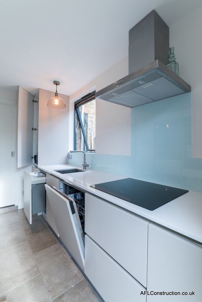 Design ideas for a mid-sized contemporary galley separate kitchen in London with a drop-in sink, flat-panel cabinets, white cabinets, solid surface benchtops, blue splashback, glass sheet splashback, stainless steel appliances, porcelain floors and no island.