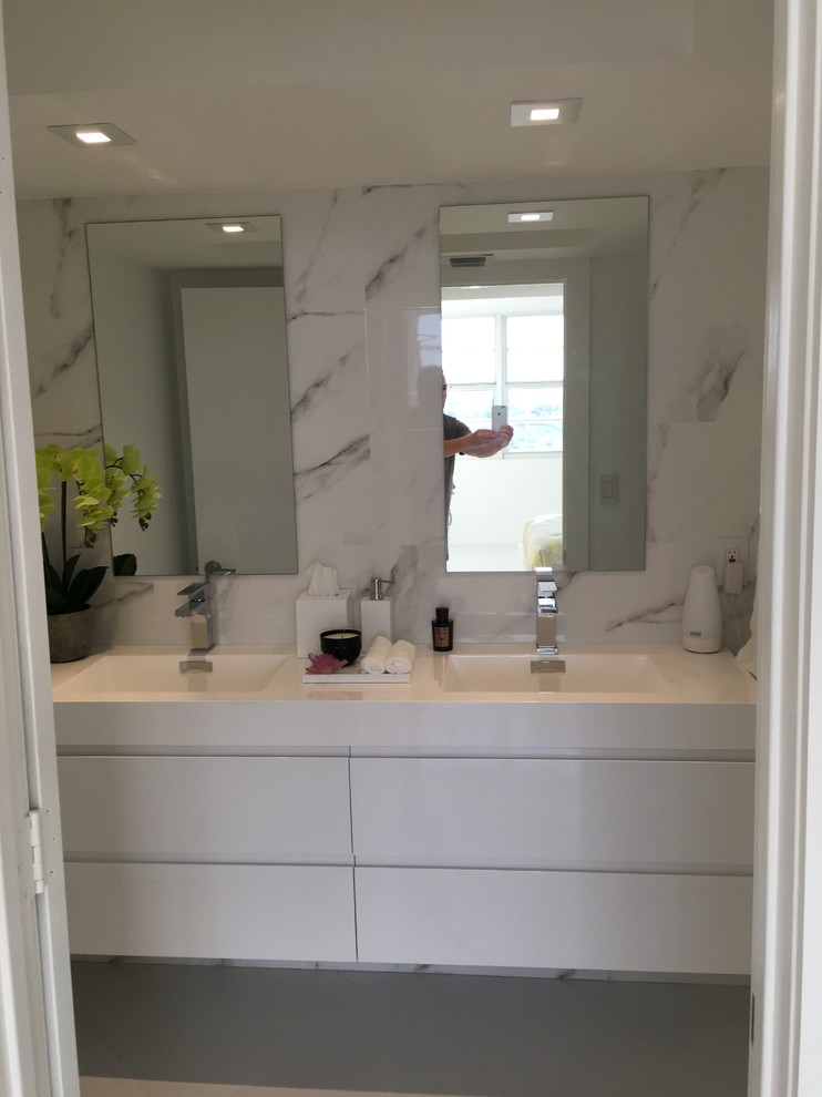 Inspiration for a mid-sized modern master bathroom in Miami with flat-panel cabinets, white cabinets, a drop-in tub, a shower/bathtub combo, a one-piece toilet, white tile, porcelain tile, white walls, porcelain floors, an integrated sink, engineered quartz benchtops, white floor and a sliding shower screen.