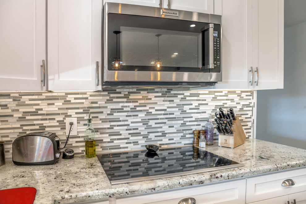 Example of a mid-sized transitional u-shaped laminate floor and brown floor open concept kitchen design in Phoenix with an undermount sink, recessed-panel cabinets, white cabinets, granite countertops, multicolored backsplash, mosaic tile backsplash and stainless steel appliances
