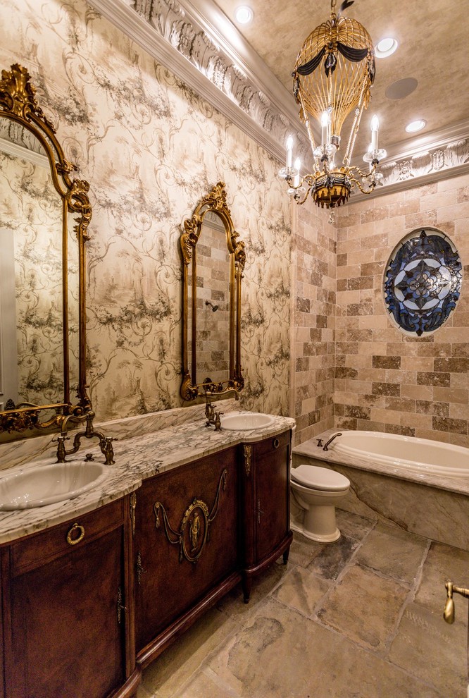 Mid-sized traditional bathroom in New Orleans with furniture-like cabinets, dark wood cabinets, a drop-in tub, a shower/bathtub combo, a one-piece toilet, beige tile, travertine, beige walls, slate floors, a drop-in sink, marble benchtops, grey floor and multi-coloured benchtops.