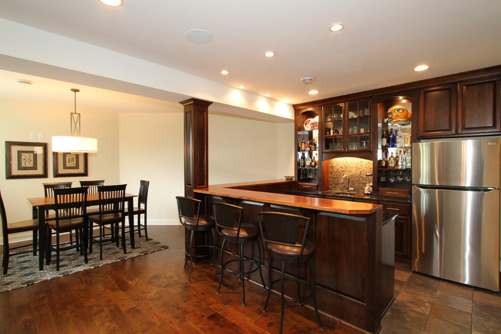 Design ideas for a mid-sized transitional u-shaped seated home bar in Milwaukee with an undermount sink, raised-panel cabinets, dark wood cabinets, wood benchtops, multi-coloured splashback, mosaic tile splashback, slate floors and brown floor.