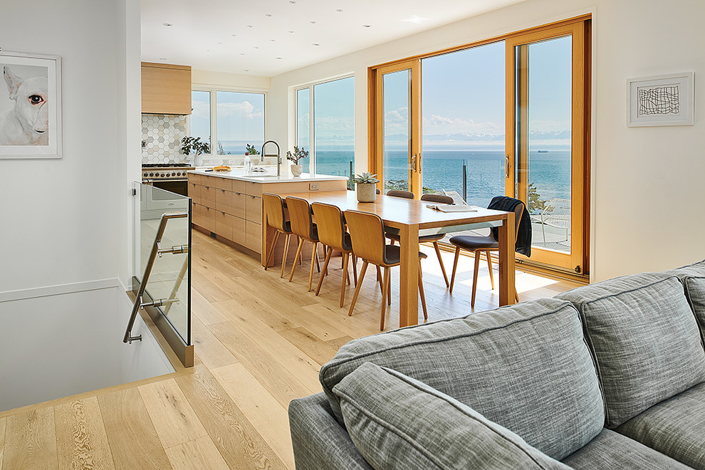 This is an example of a mid-sized modern l-shaped open plan kitchen in Other with a single-bowl sink, flat-panel cabinets, light wood cabinets, quartz benchtops, multi-coloured splashback, ceramic splashback, stainless steel appliances, light hardwood floors, with island and white benchtop.