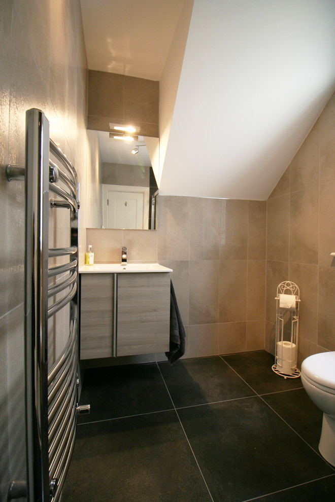 Photo of a mid-sized contemporary bathroom in Dublin with furniture-like cabinets, light wood cabinets, a corner shower, a one-piece toilet, gray tile, porcelain tile, grey walls and porcelain floors.