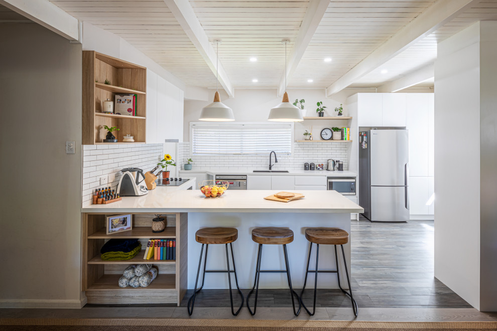 Inspiration for a contemporary u-shaped kitchen in Sydney with an undermount sink, flat-panel cabinets, white cabinets, white splashback, stainless steel appliances, dark hardwood floors, a peninsula, brown floor, white benchtop and exposed beam.