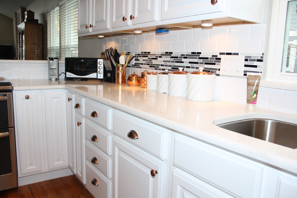 Example of a mid-sized transitional l-shaped light wood floor eat-in kitchen design in Denver with raised-panel cabinets, white cabinets, stainless steel appliances, an island, an undermount sink, quartz countertops, multicolored backsplash and glass tile backsplash