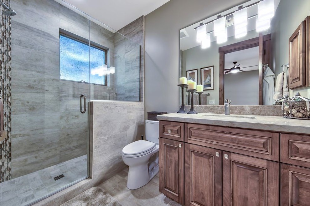 Example of a mid-sized transitional 3/4 porcelain tile and gray floor alcove shower design with medium tone wood cabinets, a one-piece toilet, gray walls, an undermount sink, quartzite countertops, a hinged shower door and gray countertops