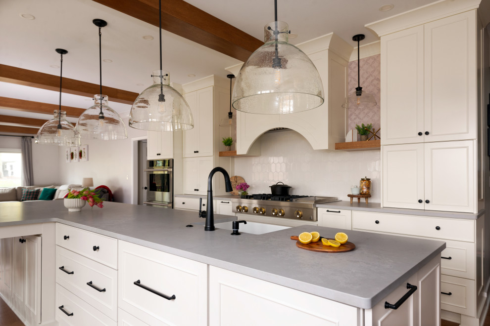 Example of a large medium tone wood floor and exposed beam eat-in kitchen design with white backsplash, stainless steel appliances and an island