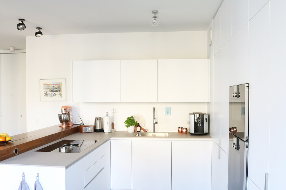 Inspiration for a mid-sized contemporary u-shaped open plan kitchen in Berlin with flat-panel cabinets, white cabinets, solid surface benchtops, white splashback, black appliances, bamboo floors, no island and white floor.