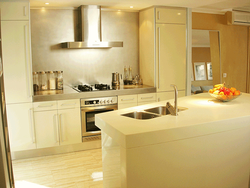 This is an example of a contemporary open plan kitchen in Alicante-Costa Blanca with flat-panel cabinets, yellow cabinets, solid surface benchtops, metallic splashback, porcelain floors, with island, multi-coloured floor and yellow benchtop.