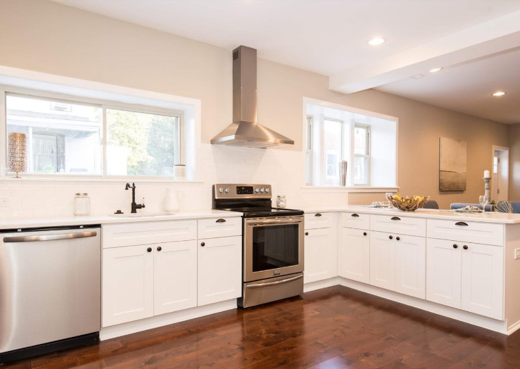 Mid-sized transitional l-shaped medium tone wood floor and brown floor open concept kitchen photo in Philadelphia with an undermount sink, shaker cabinets, white cabinets, quartz countertops, stainless steel appliances and a peninsula