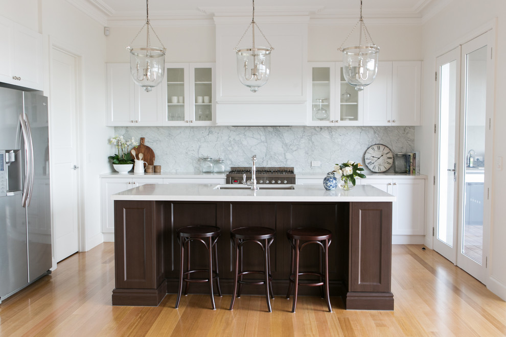 This is an example of a traditional l-shaped kitchen in Melbourne with an undermount sink, shaker cabinets, white cabinets, white splashback, stainless steel appliances, light hardwood floors and with island.
