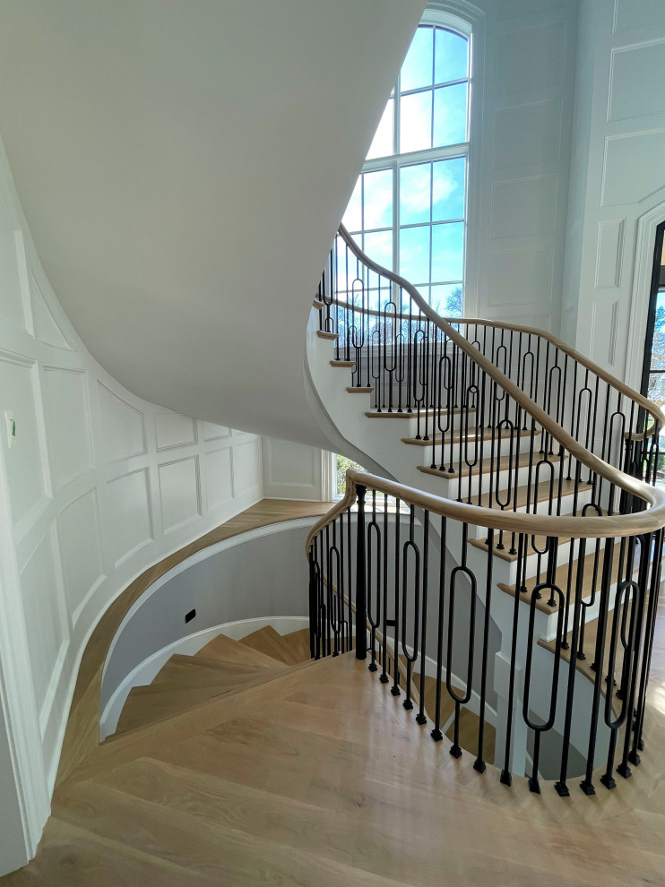 Photo of an expansive classic wood curved mixed railing staircase in DC Metro with wood risers and wainscoting.