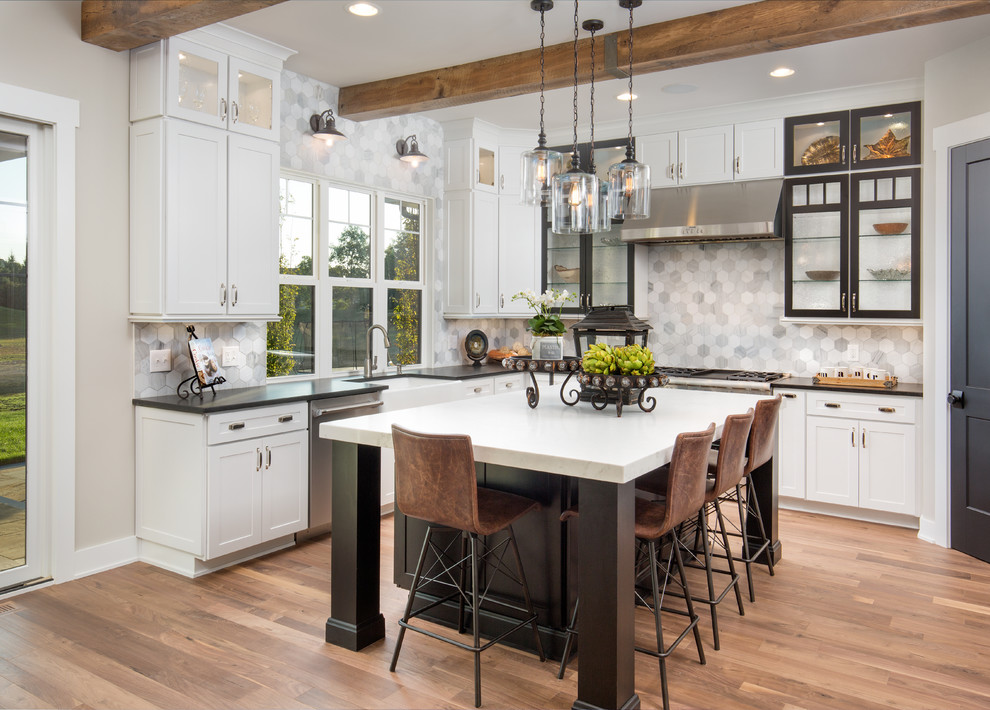 Design ideas for a country u-shaped kitchen in Columbus with a farmhouse sink, shaker cabinets, white cabinets, grey splashback, stainless steel appliances, medium hardwood floors, with island, brown floor and black benchtop.