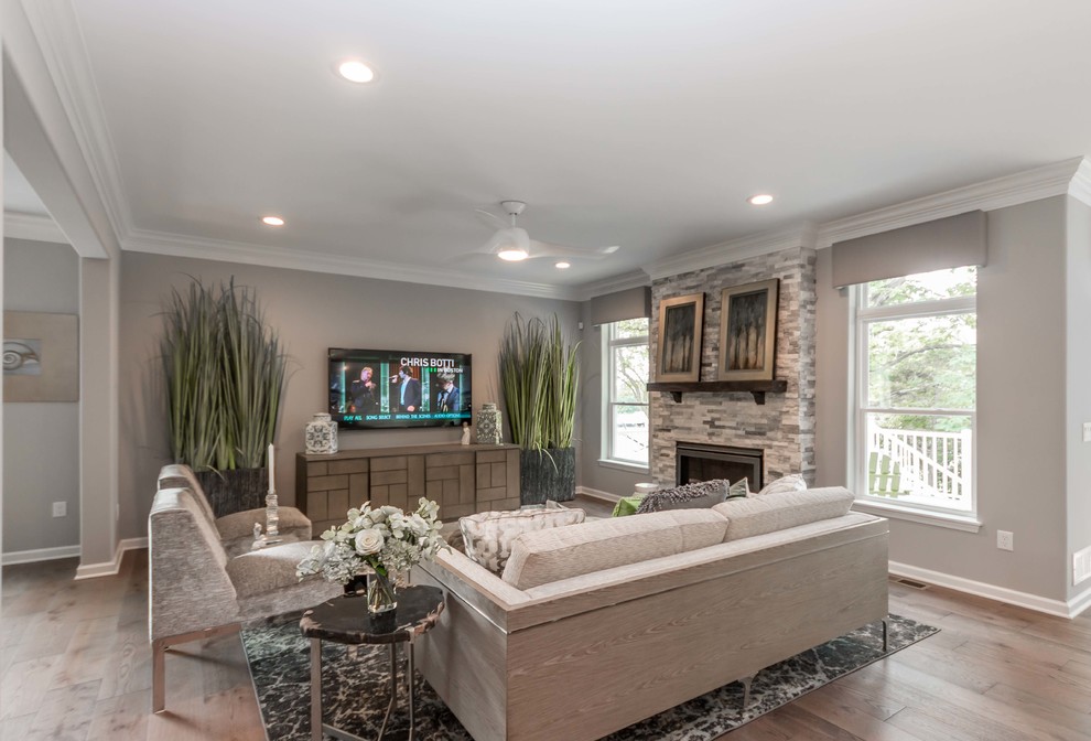 This is an example of a mid-sized transitional open concept family room in Milwaukee with grey walls, medium hardwood floors, a standard fireplace, a stone fireplace surround, a wall-mounted tv and brown floor.