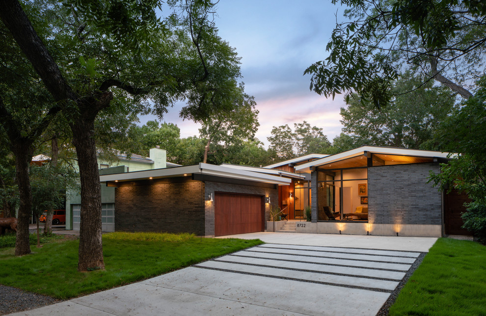 Small midcentury one-storey brick black house exterior in Dallas with a gable roof and a metal roof.