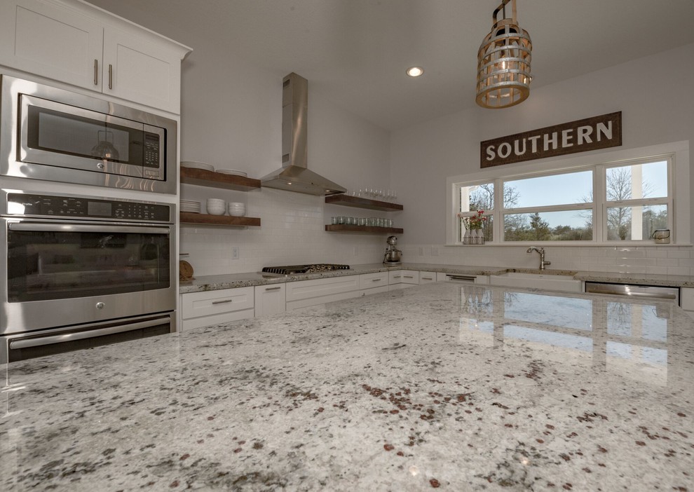 Mid-sized country u-shaped open plan kitchen in Austin with a farmhouse sink, shaker cabinets, white cabinets, granite benchtops, white splashback, subway tile splashback, stainless steel appliances, concrete floors, with island and grey floor.