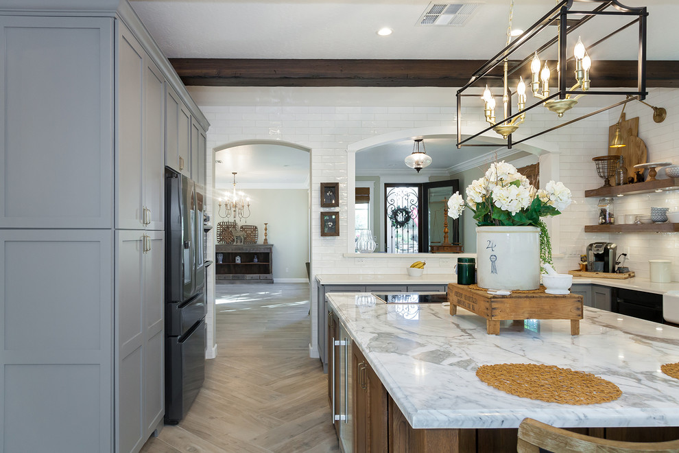 Inspiration for a large transitional l-shaped porcelain tile and brown floor eat-in kitchen remodel in Phoenix with a farmhouse sink, shaker cabinets, gray cabinets, quartz countertops, white backsplash, glass sheet backsplash, stainless steel appliances, an island and white countertops