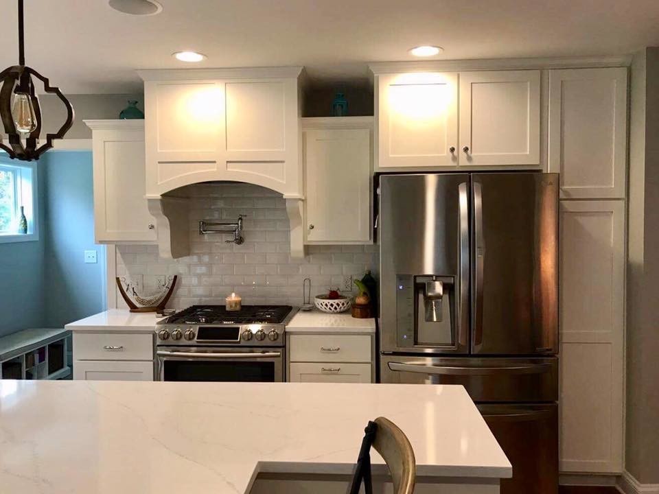 Transitional l-shaped kitchen photo in Philadelphia with a farmhouse sink, shaker cabinets, white cabinets, marble countertops, white backsplash, subway tile backsplash, stainless steel appliances and an island