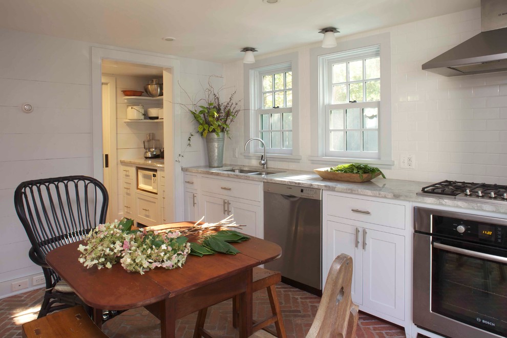 Photo of a country eat-in kitchen in New York with a double-bowl sink, shaker cabinets, white cabinets, white splashback, subway tile splashback, stainless steel appliances, marble benchtops and brick floors.