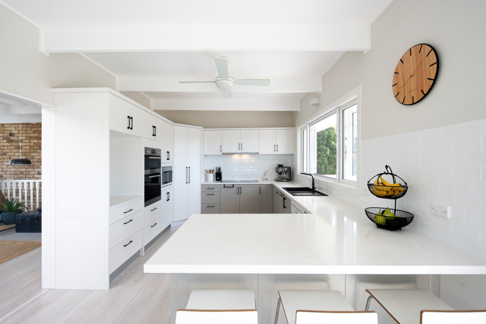 Inspiration for a mid-sized contemporary u-shaped kitchen pantry in Sydney with shaker cabinets, white cabinets, quartz benchtops, white splashback, ceramic splashback, stainless steel appliances, a peninsula and white benchtop.