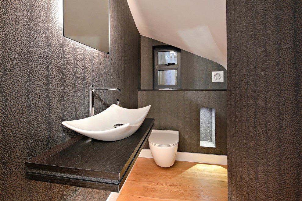Small contemporary powder room in Hertfordshire with a wall-mount toilet, grey walls, light hardwood floors, a wall-mount sink, wood benchtops and brown benchtops.