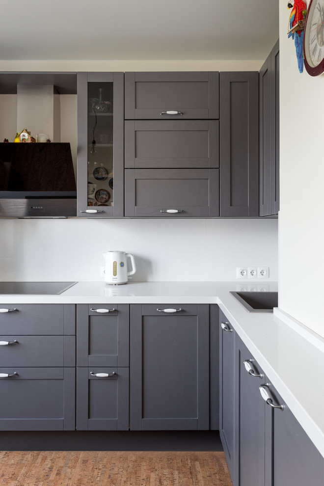 This is an example of a mid-sized scandinavian l-shaped separate kitchen in Moscow with a drop-in sink, shaker cabinets, grey cabinets, quartz benchtops, white splashback, stone slab splashback, black appliances, cork floors, no island, brown floor and white benchtop.