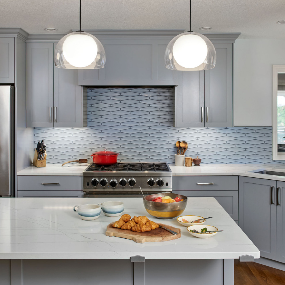 Design ideas for a mid-sized transitional l-shaped open plan kitchen in Portland with an undermount sink, shaker cabinets, blue cabinets, blue splashback, ceramic splashback, stainless steel appliances, medium hardwood floors, with island, brown floor and white benchtop.
