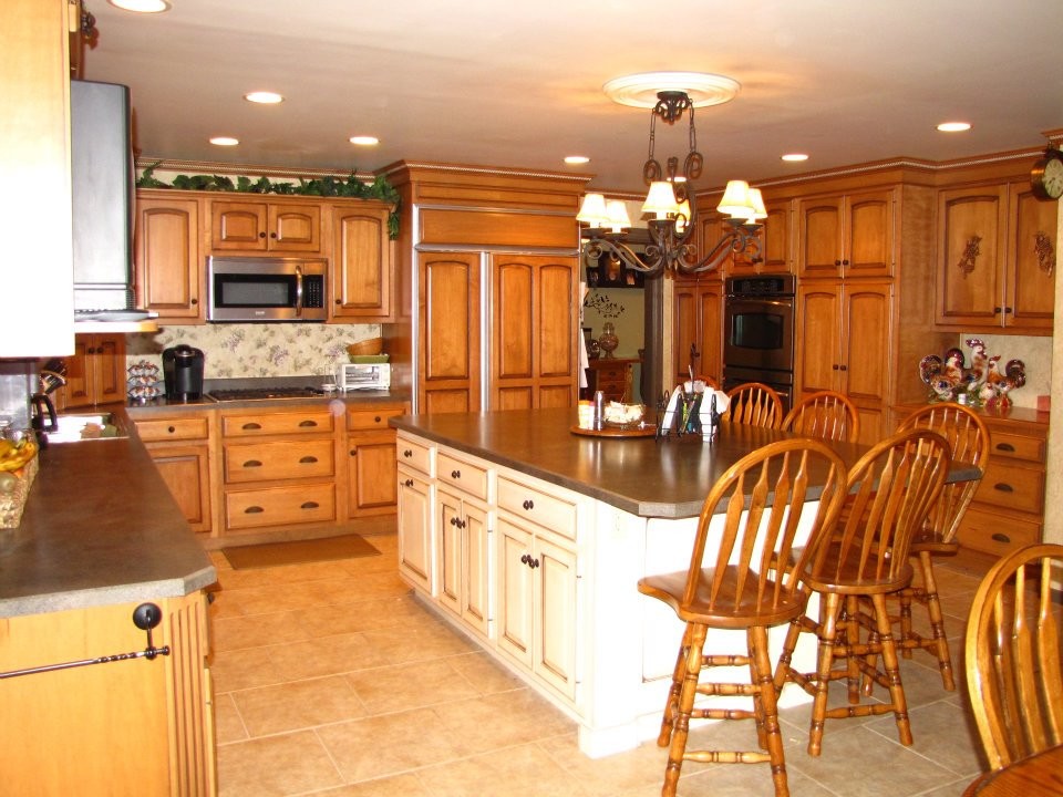 Large minimalist u-shaped ceramic tile and brown floor eat-in kitchen photo with a drop-in sink, raised-panel cabinets, medium tone wood cabinets, stainless steel appliances and an island