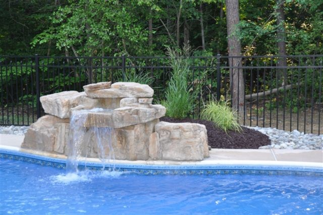 Photo of a mid-sized tropical backyard custom-shaped pool in DC Metro with a water feature and concrete slab.