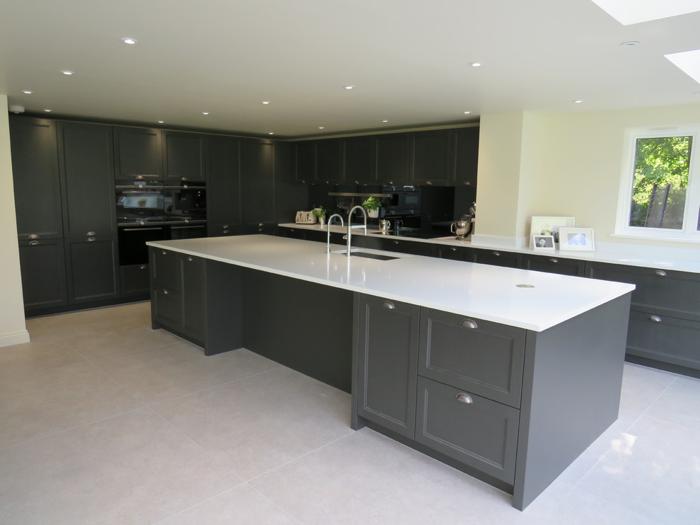 Large contemporary l-shaped open plan kitchen in Essex with an integrated sink, shaker cabinets, grey cabinets, quartzite benchtops, metallic splashback, glass sheet splashback, black appliances, ceramic floors, with island, grey floor and white benchtop.