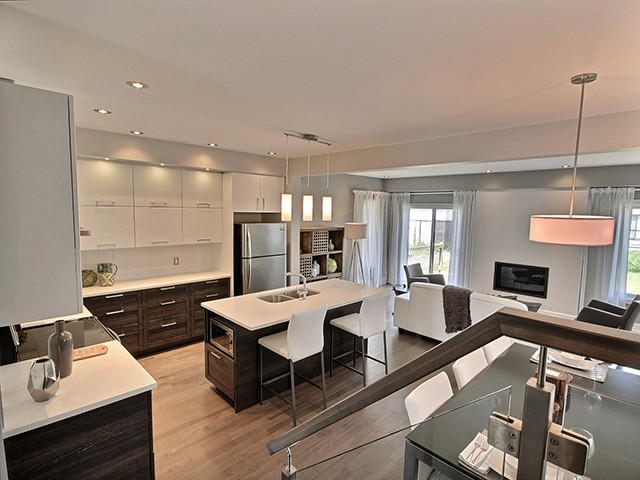 This is an example of a small contemporary l-shaped eat-in kitchen in Ottawa with white cabinets, quartzite benchtops, white splashback, with island, an undermount sink, flat-panel cabinets, ceramic splashback, stainless steel appliances, medium hardwood floors and brown floor.