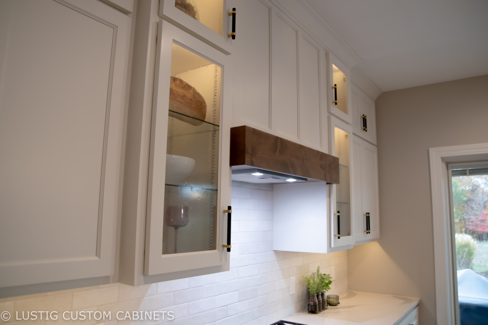 Example of a large transitional l-shaped laminate floor and brown floor open concept kitchen design with an undermount sink, flat-panel cabinets, white cabinets, quartz countertops, white backsplash, ceramic backsplash, stainless steel appliances, an island and white countertops