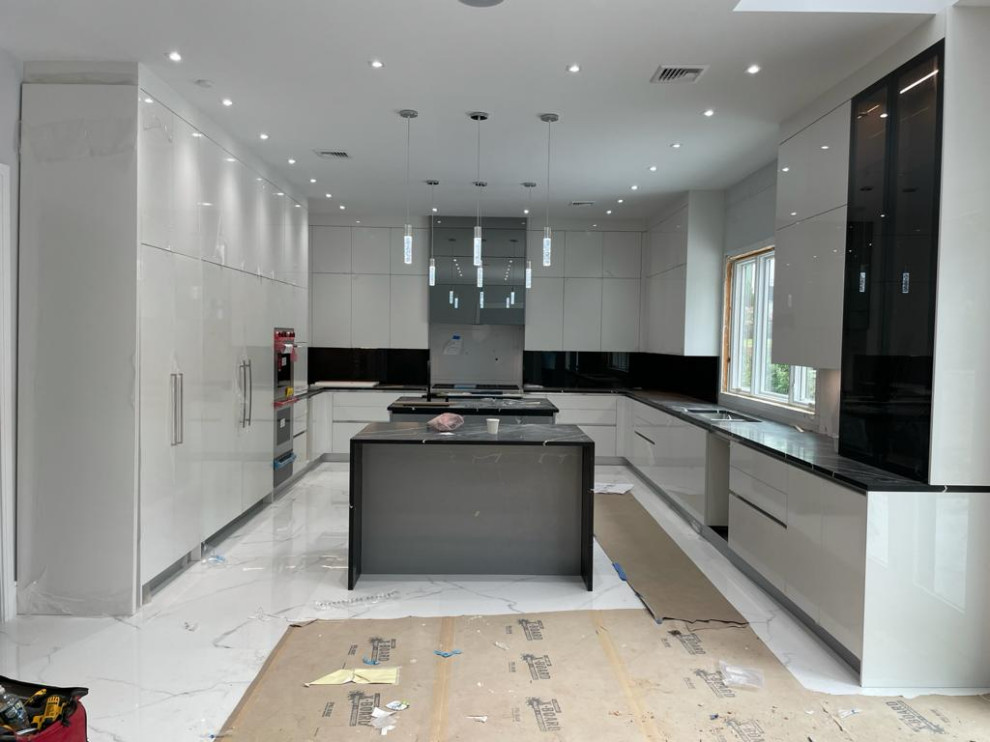 Inspiration for an expansive contemporary u-shaped kitchen/diner in New York with a double-bowl sink, flat-panel cabinets, white cabinets, engineered stone countertops, black splashback, engineered quartz splashback, integrated appliances, porcelain flooring, multiple islands, white floors and black worktops.