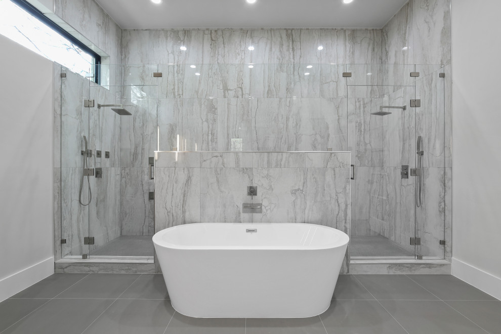 This is an example of a large modern master bathroom in Dallas with flat-panel cabinets, light wood cabinets, a freestanding tub, a double shower, a one-piece toilet, gray tile, porcelain tile, white walls, porcelain floors, an undermount sink, engineered quartz benchtops, grey floor, a hinged shower door, white benchtops, a shower seat, a double vanity and a built-in vanity.