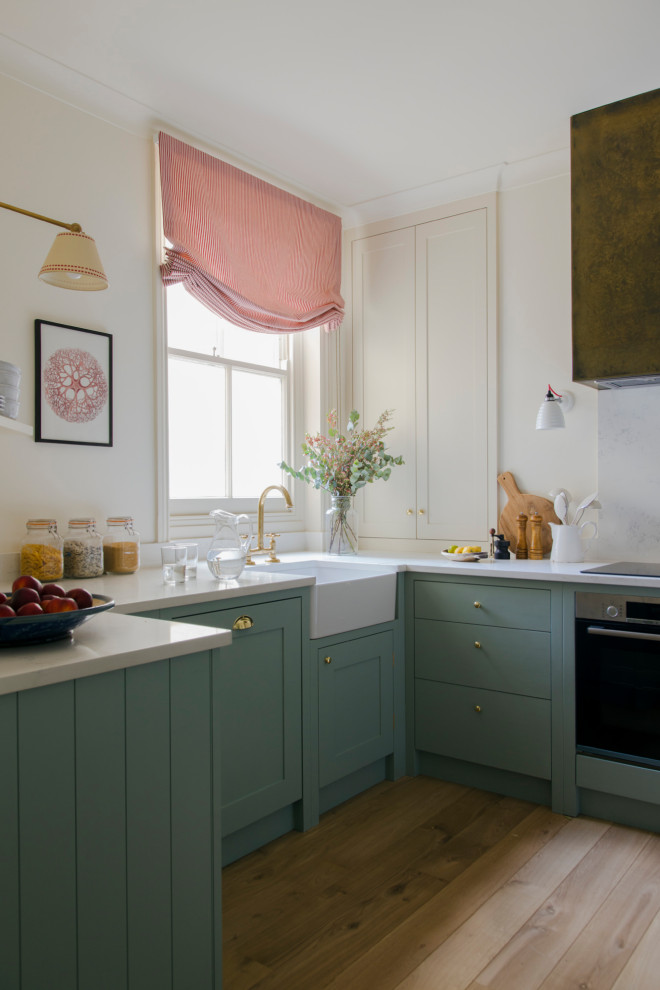 Design ideas for a medium sized victorian l-shaped enclosed kitchen in London with a belfast sink, flat-panel cabinets, blue cabinets, quartz worktops, white splashback, black appliances, light hardwood flooring, no island, yellow worktops and a feature wall.