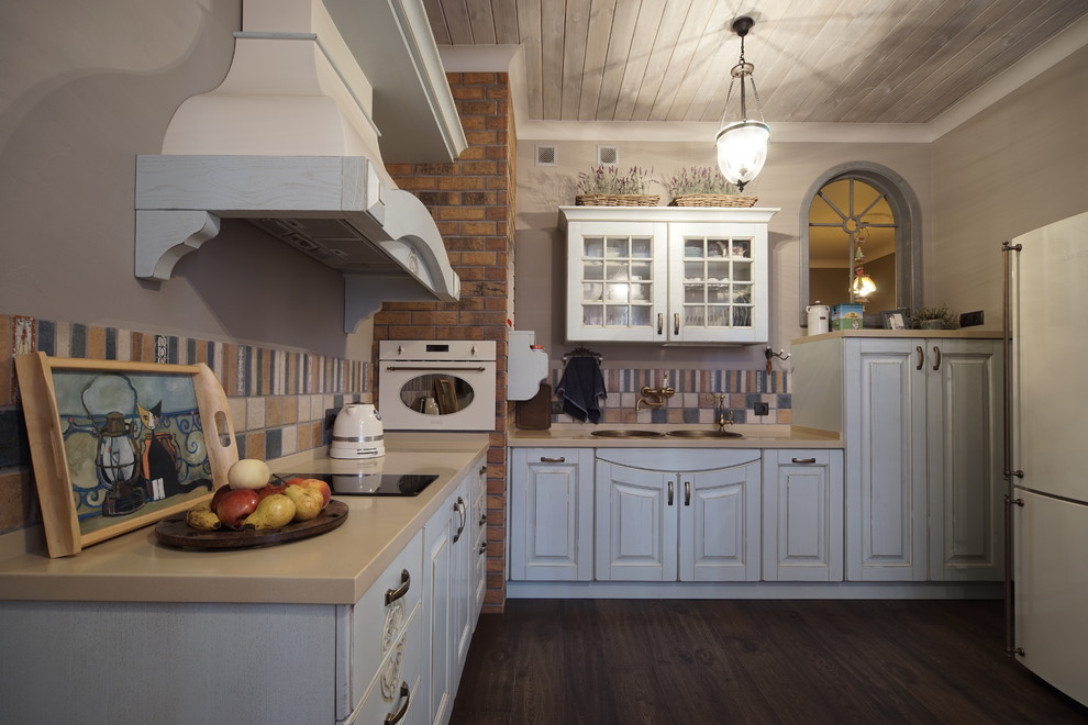 Inspiration for a large country l-shaped eat-in kitchen in Moscow with a double-bowl sink, distressed cabinets, solid surface benchtops, porcelain splashback, white appliances, dark hardwood floors, no island, recessed-panel cabinets, multi-coloured splashback, brown floor and beige benchtop.