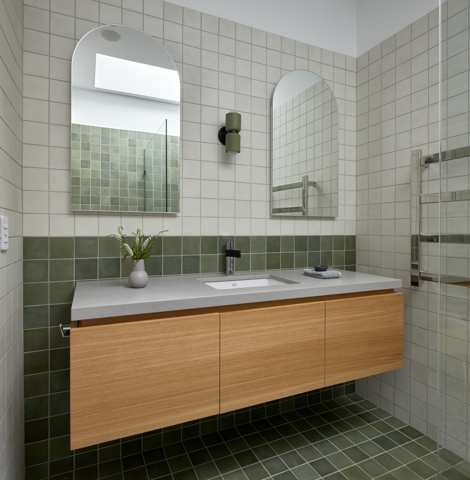 Esempio di una stanza da bagno design di medie dimensioni con ante lisce, ante in legno chiaro, piastrelle verdi, piastrelle in ceramica, pavimento con piastrelle in ceramica, lavabo sottopiano, top in superficie solida, pavimento verde, top grigio, un lavabo e mobile bagno sospeso