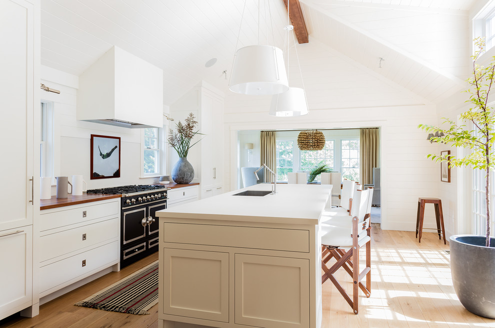This is an example of a large beach style galley kitchen in Other with an undermount sink, shaker cabinets, white cabinets, quartzite benchtops, white splashback, black appliances, light hardwood floors and with island.