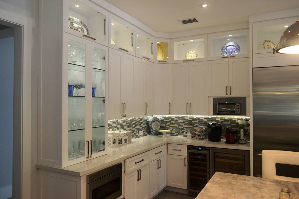 This is an example of a large transitional u-shaped separate kitchen in Miami with a farmhouse sink, shaker cabinets, white cabinets, quartzite benchtops, multi-coloured splashback, glass tile splashback, stainless steel appliances, porcelain floors and with island.