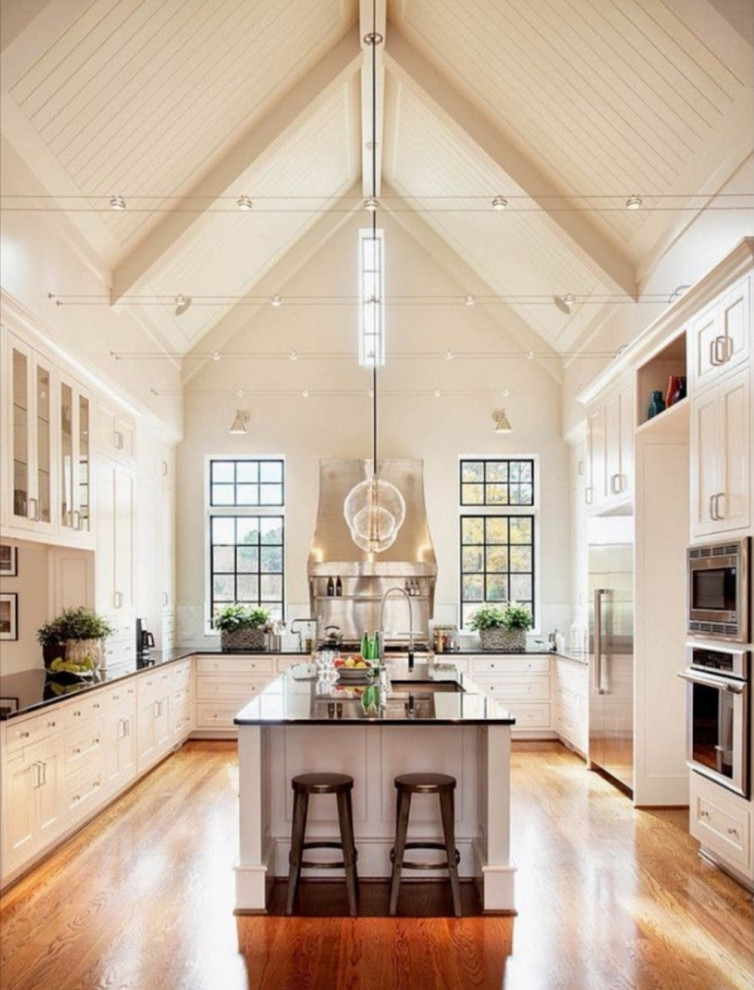 Inspiration for a large country u-shaped open plan kitchen in Other with an integrated sink, beaded inset cabinets, white cabinets, quartzite benchtops, white splashback, glass sheet splashback, stainless steel appliances, painted wood floors, with island, brown floor and black benchtop.