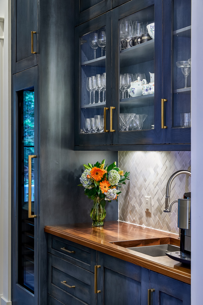 Photo of a large transitional home bar in Charleston with an undermount sink, glass-front cabinets, blue cabinets, wood benchtops, grey splashback, medium hardwood floors and brown benchtop.