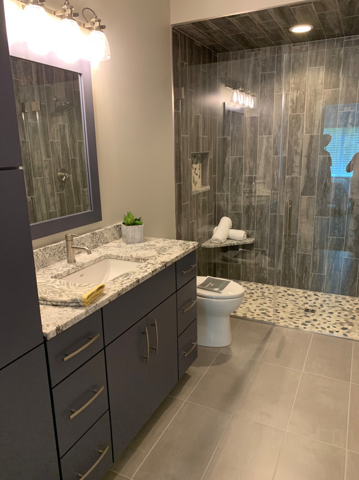 This is an example of a mid-sized contemporary 3/4 bathroom in Cleveland with flat-panel cabinets, grey cabinets, an alcove shower, a one-piece toilet, gray tile, porcelain tile, grey walls, porcelain floors, an undermount sink, quartzite benchtops, grey floor, a hinged shower door, white benchtops, a niche, a single vanity and a built-in vanity.