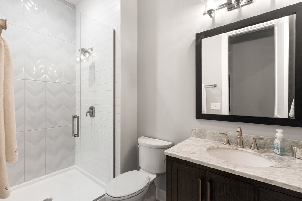 Inspiration for a mid-sized arts and crafts bathroom in Columbus with recessed-panel cabinets, dark wood cabinets, an alcove shower, a two-piece toilet, white tile, subway tile, grey walls, an undermount sink, marble benchtops, a hinged shower door and grey benchtops.